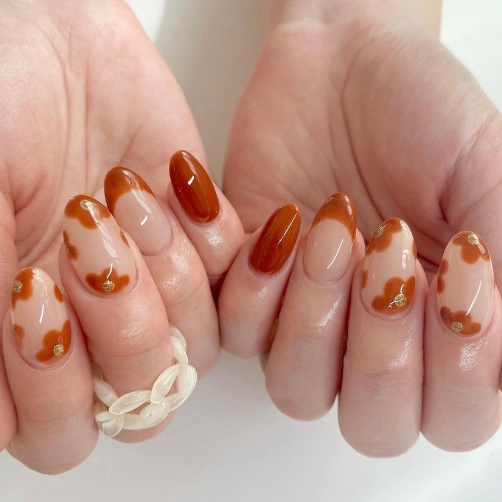 A simple nail design with burnt orange flowers and French tips