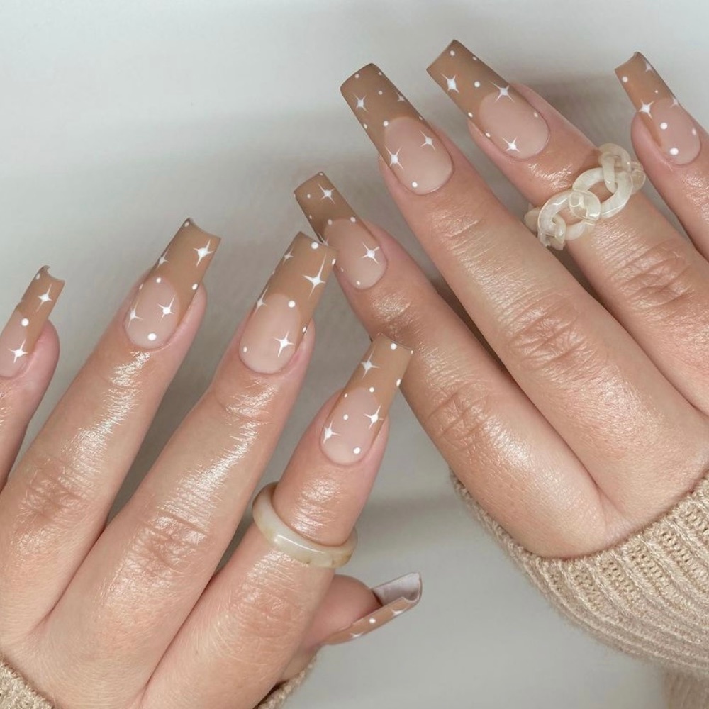 Long acrylic nails with tan French tips and white stars all over the nails