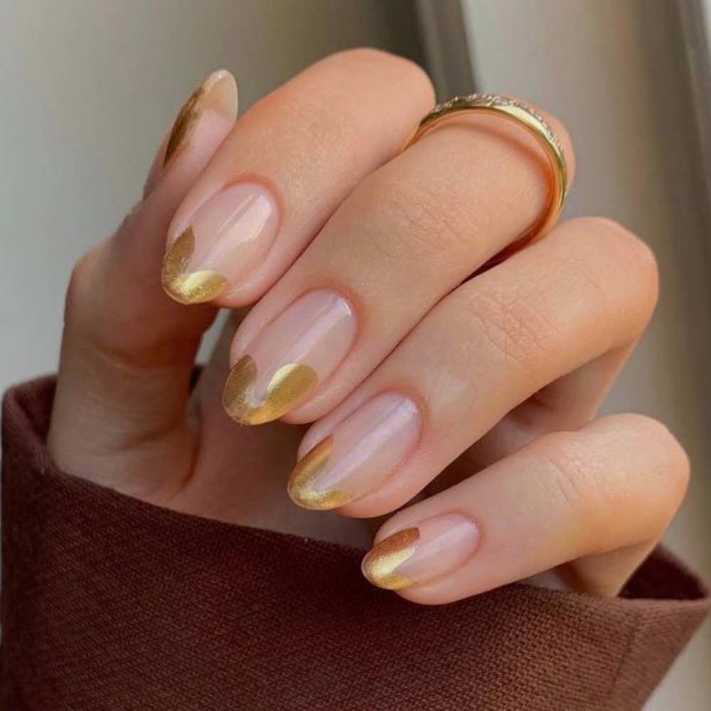 Almond shaped nails with a curvy french tip in a gold color